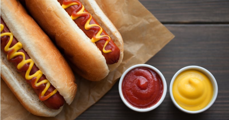deux hot-dog sur un papier et deux sauce tomate et moutarde